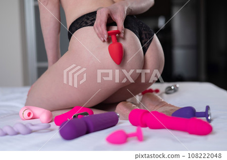 Close-up of female buttocks and sex toys on the bed. Woman holding anal plug.  108222048
