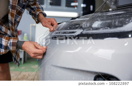Male master in car service applying protective armor film to car body 108222897