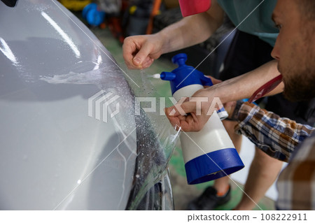 Closeup concentrated man worker smoothing protective film in car garage 108222911