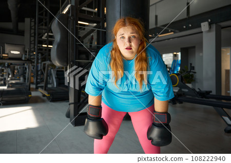Portrait of pretty young woman with excess weight in boxing gloves feeling tired 108222940
