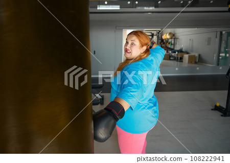 Concentrated fat woman using boxing gloves doing punching exercises 108222941