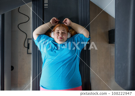Sad unhappy overweight woman feeling pain while training at wall for posture correction Sad unhappy overweight woman feeling pain while training at wall for posture correction 108222947