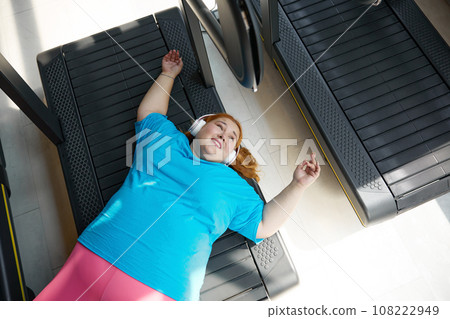 High angle view on happy but tired overweight woman lying on treadmill machine track 108222949