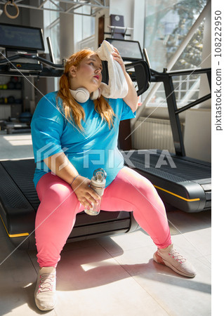 Tired plus size girl wiping sweat from her face feeling exhaustion after training 108222950