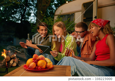 Happy teen friends spending evening nearby bonfire and campsite Happy teen friends spending evening nearby bonfire and campsite 108223000