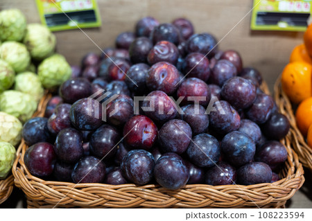 Ripe juicy plums in wicker box on supermarket shelf 108223594