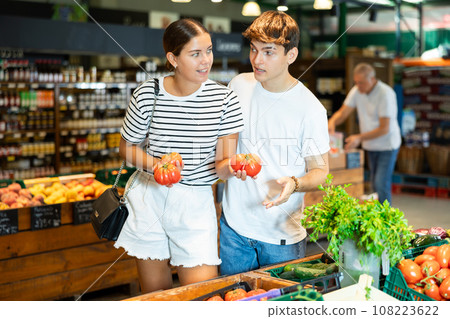 Young couple choosing ripe tomatoes in vegetable section of supermarket 108223622