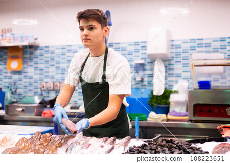 Positive salesman demonstrating sole fish behind counter in shop 108223651