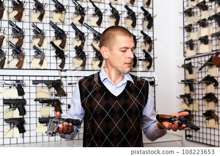 Man examining sporting revolvers before buying in gun store Man examining sporting revolvers before buying in gun store 108223653