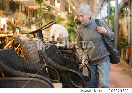 Senior woman looking for plastic rattan garden furniture in store 108223731