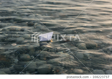 White paper boat floats on water with waves and ripples. White paper boat floats on water with waves and ripples. 108223737