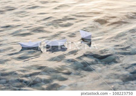 Three paper boats floating in waves on the water at sunset. Three paper boats floating in waves on the water at sunset. 108223750