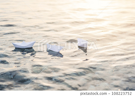 Three paper boats floating in waves on the water at sunset. Three paper boats floating in waves on the water at sunset. 108223752