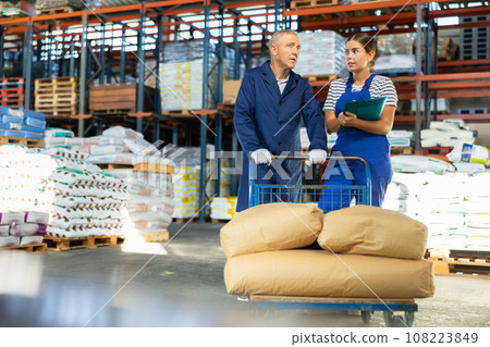 Girl checks papers invoices with mature man employee and revise availability of sacks goods in stock Girl checks papers invoices with mature man employee and revise availability of sacks goods in stock 108223849