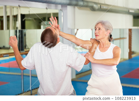 Elderly woman is training with man on self-defense course in gym 108223913