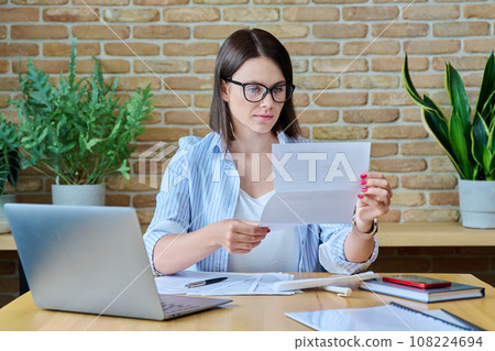 Serious young business woman reading official letter, sitting in office 108224694