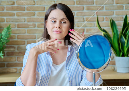 Young happy brunette looking at her face in mirror Young happy brunette looking at her face in mirror 108224695