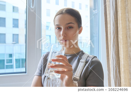 Close-up of teenage girl drinking water from glass, at home Close-up of teenage girl drinking water from glass, at home 108224696