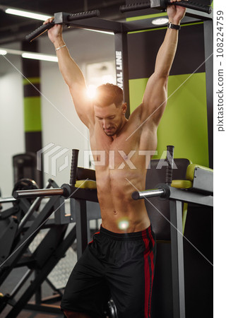Attractive guy doing pull-up on the crossbar during training in the modern gym. Close up shot. 108224759
