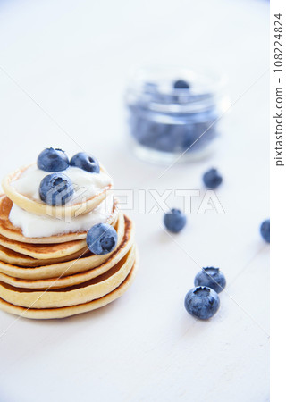 Delicious homemade pancakes with yogurt and fresh blueberries on white wooden background. Delicious homemade pancakes with yogurt and fresh blueberries on white wooden background. 108224824