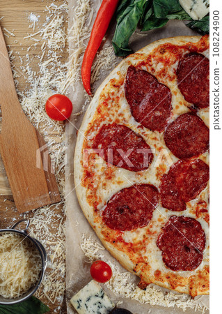 Pizza with chicken cheese and pepperoni, a piece of which is cut and laid out like a pakman, is on a wooden board and a brown background. Cheese spreads flowing streaks Pizza with chicken cheese and pepperoni, a piece of which is cut and laid out like a pakman, is on a wooden board and a brown background. Cheese spreads flowing streaks 108224900