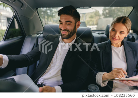 Smiling business analysts have online meeting using laptop while sitting in car back seats 108225560