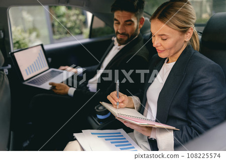 Business colleagues working on laptop and making notes while sitting in car backseats  108225574