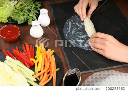 Woman making rice paper roll at wooden table, closeup 108225662