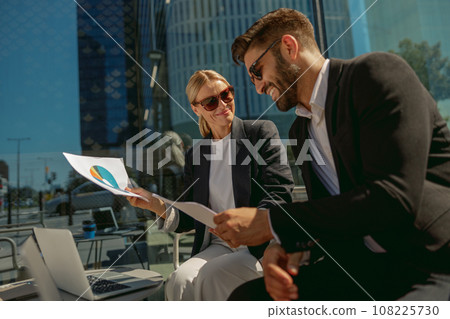 Two business partners working with documents sitting outside of office on cafe terrace Two business partners working with documents sitting outside of office on cafe terrace 108225730