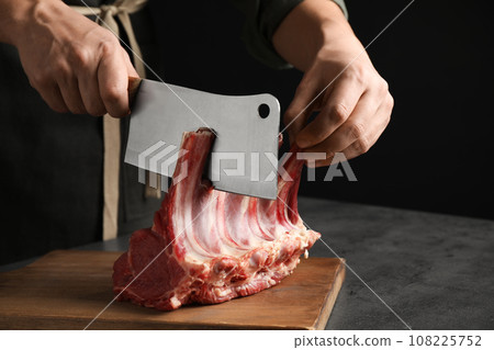 Man cutting raw ribs at grey table, closeup Man cutting raw ribs at grey table, closeup 108225752
