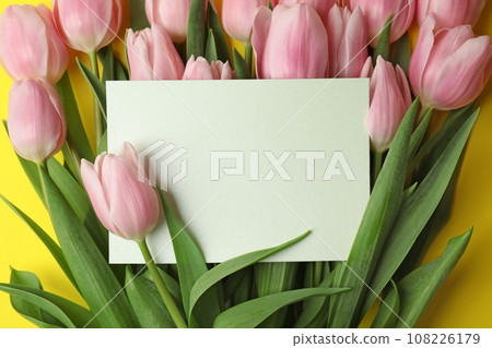 Beautiful pink spring tulips and blank card on yellow background, closeup. Space for text 108226179
