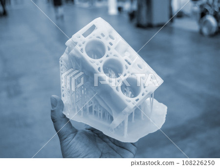 Person holding in palm of hand prototype of car engine printed on 3D printer from molten white plastic. Three-dimensional model. Additive progressive modeling technology. Modern new printing industry. Person holding in palm of hand prototype of car engine printed on 3D printer from molten white plastic. Three-dimensional model. Additive progressive modeling technology. Modern new printing industry. 108226250