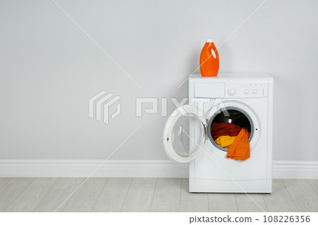 Modern washing machine with laundry and detergent near white wall. Space for text 108226356