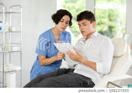 Young male patient signing papers while talking with woman doctor 108227203