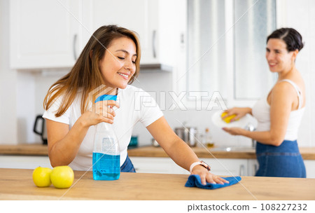 Positive young Latina cleaning home kitchen with sister Positive young Latina cleaning home kitchen with sister 108227232