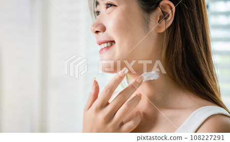 Asian beautiful young woman applying cosmetic cream on neck at home, Happy female apply lotion moisturizer on her neck after shower, Beauty skin care cosmetic protect and nourish skin concept 108227291