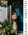 A stylish woman with a baby in her arms. A baby in his mother's arms. A beautiful portrait of a child in the arms of his mother. Mom hugs the baby. A woman with a baby on the background of the door 108227543