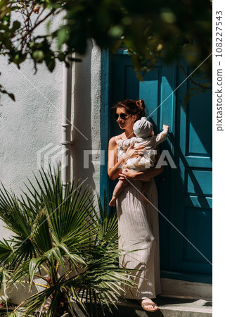 A stylish woman with a baby in her arms. A baby in his mother's arms. A beautiful portrait of a child in the arms of his mother. Mom hugs the baby. A woman with a baby on the background of the door A stylish woman with a baby in her arms. A baby in his mother's arms. A beautiful portrait of a child in the arms of his mother. Mom hugs the baby. A woman with a baby on the background of the door 108227543