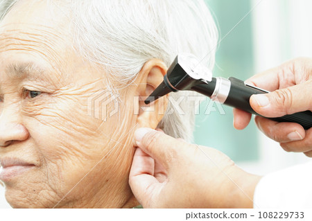 Otolaryngologist or ENT physician doctor examining senior patient ear with otoscope, hearing loss problem. Otolaryngologist or ENT physician doctor examining senior patient ear with otoscope, hearing loss problem. 108229733
