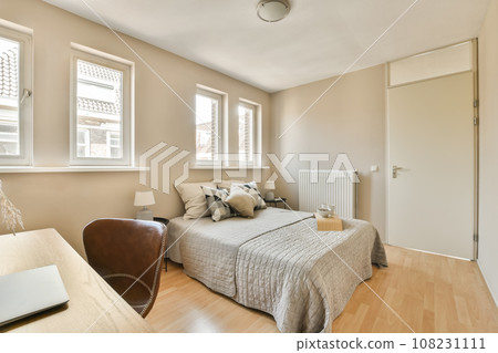 a bedroom with a bed, desk and laptop on the table in front of the window looking out to the street 108231111