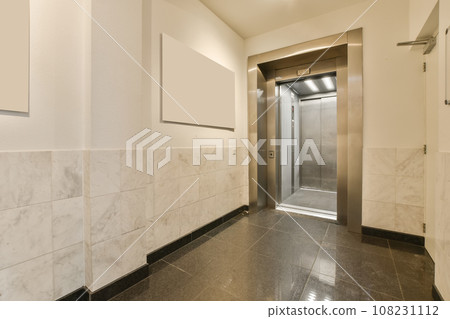 an elevator room with marble flooring and white wall tiles on the walls there is a stainless door in the background 108231112