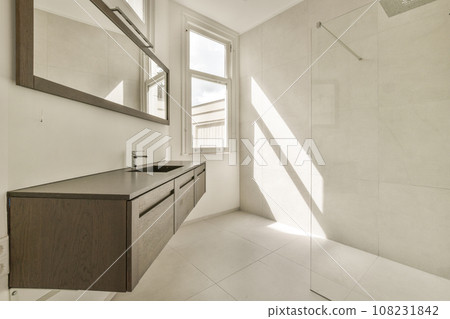 a bathroom with white tile and wood cabinetd vanity in the corner, looking out to the outside through the window 108231842