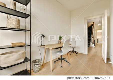a home office with white walls and wood flooring the room is well lit by natural light from the windows 108232684