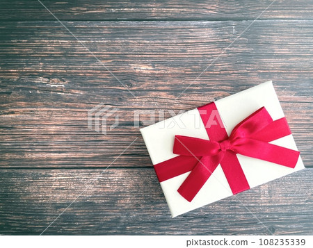 Present box with red ribbon placed on wooden table 108235339