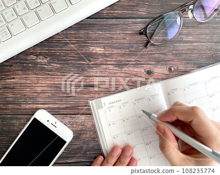 A woman's hand filling out a schedule book at her desk 108235774