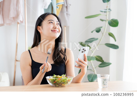 A young woman eating a salad while looking at her smartphone A young woman eating a salad while looking at her smartphone 108236995