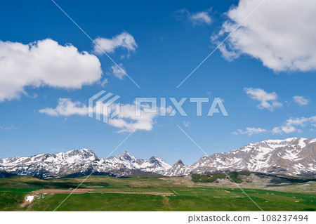 High snow-capped mountain range over sunny green valley High snow-capped mountain range over sunny green valley 108237494