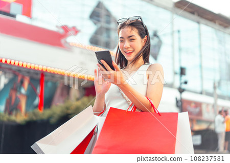 Asian woman city lifestyles using smartphone standing at outdoor with shopping bags 108237581