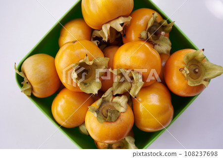 Full rhombic bowl of orange persimmons on a white table. Top view 108237698