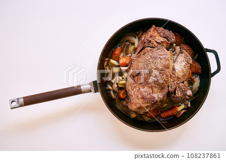Frying pan with a wooden handle with roast beef and vegetables on a white table. Top view 108237861